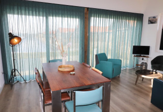 Luminoso interior de lodge en los Países Bajos con cortinas azuladas, mesa de madera y mobiliario moderno.