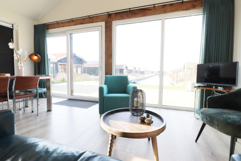Lys og moderne stue i en lodge ved vandet, med store vinduer og hyggelige siddepladser i Holland.