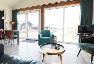 Lys og moderne stue i en lodge ved vandet, med store vinduer og hyggelige siddepladser i Holland.