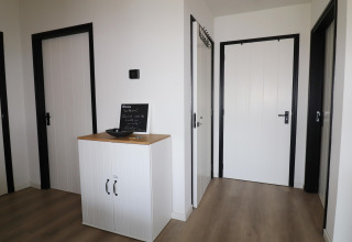 Entré på lodge i Holland med lyse trægulve, hvide døre og sort kant, lille skab og velkomsttavle.