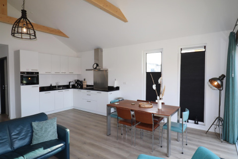 Alojamiento moderno en los Países Bajos con cocina abierta, mesa de comedor y vigas de madera.