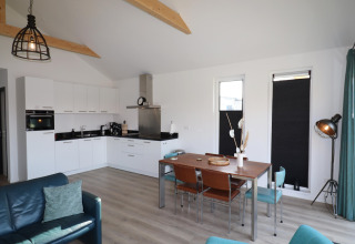 Alojamiento moderno en los Países Bajos con cocina abierta, mesa de comedor y vigas de madera.