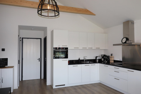 Cocina moderna blanca con encimeras negras y madera a la vista en Scenic Stay with Lodge, Países Bajos.