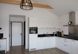 Cocina moderna blanca con encimeras negras y madera a la vista en Scenic Stay with Lodge, Países Bajos.
