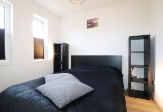 Habitación moderna en 'Scenic Stay with' en Países Bajos con cama negra, estantes y dos ventanas luminosas.