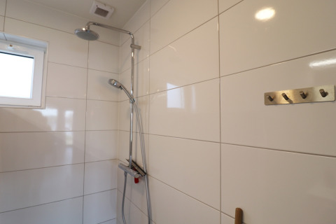 Ducha moderna con paredes de azulejos blancos, ganchos en la pared y ventana, en Scenic Stay with, Países Bajos.