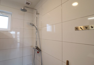 Ducha moderna con paredes de azulejos blancos, ganchos en la pared y ventana, en Scenic Stay with, Países Bajos.
