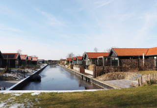 Scenic Stay with hytter ved en kanalside i Holland, omgivet af sne og grønne områder under blå himmel.