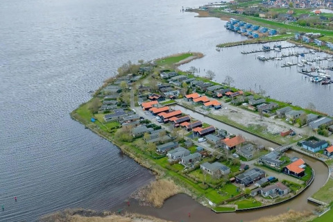 Luftfoto af ferieboliger ved en sø i Holland med bådehavn og grønne omgivelser en overskyet dag.
