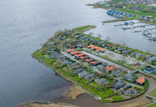 Luftfoto af ferieboliger ved en sø i Holland med bådehavn og grønne omgivelser en overskyet dag.