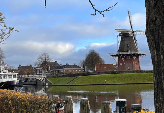 Molino de viento junto al canal con botes, árboles y casas al fondo, en Scenic Stay with en los Países Bajos.