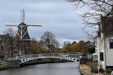 Molino de viento y puente de canal junto al alojamiento 'Scenic Stay with' en Países Bajos en día nublado.