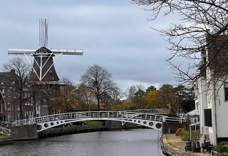Molino de viento y puente de canal junto al alojamiento 'Scenic Stay with' en Países Bajos en día nublado.