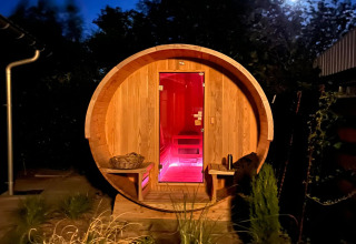 Sauna redonda de madera con iluminación roja de noche en la cabaña 'Scenic Stay with' en los Países Bajos.