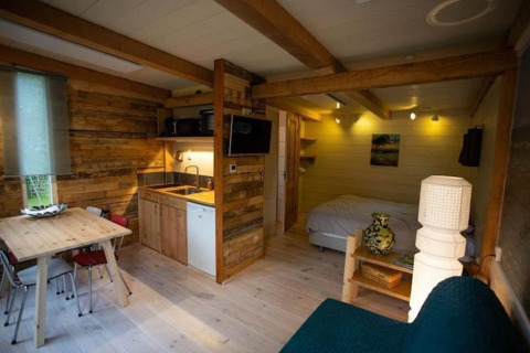 Hyggelig chalet i Sint Maartenszee, Holland med træinteriør, tekøkken og spisebord tæt på sengen.