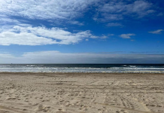 Uitzicht vanop een strandhuis met zand, rustige zee en blauwe lucht met wat verspreide wolken.