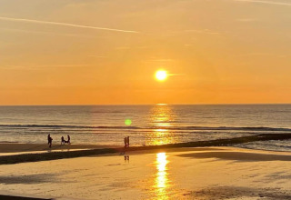 Sonnenuntergang am Meer, aufgenommen von einem Strandhaus, mit Spaziergängern am Ufer im Abendlicht.