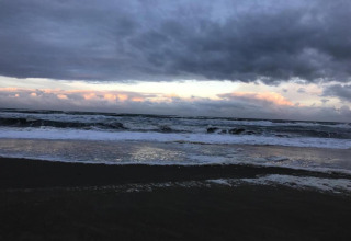 Vue d'une plage agitée avec de gros nuages sombres, des vagues mousseuses et un rayon de soleil lointain.