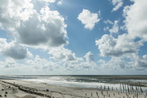Strandzicht met golven, zand en wolken, overdag gefotografeerd vanuit een strandhuis aan de kust.