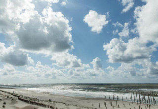 Strandzicht met golven, zand en wolken, overdag gefotografeerd vanuit een strandhuis aan de kust.