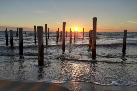 Solnedgang over havet med mange træpæle i vandet ved stranden, taget fra et strandhus.