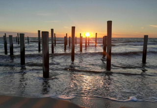 Coucher de soleil sur l’océan avec de nombreux poteaux en bois dans l’eau, vu depuis une maison de plage.