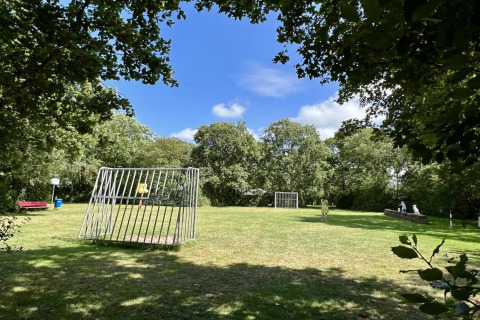 Groen grasveld met spelende kinderen, twee voetbaldoelen en bomen bij een chalet in Nederland.