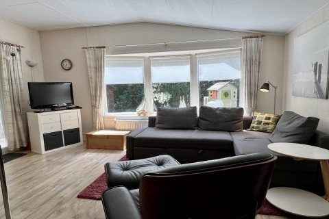 Salon d’un petit chalet familial proche de la plage aux Pays-Bas, avec canapé, télévision et grandes fenêtres.
