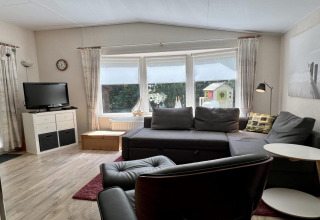 Salon d’un petit chalet familial proche de la plage aux Pays-Bas, avec canapé, télévision et grandes fenêtres.