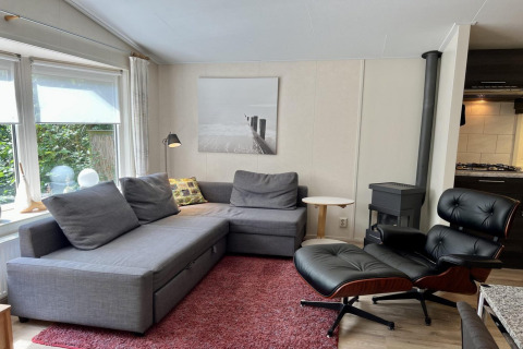 Knusse woonkamer van een klein familiechalet nabij het strand in Nederland met grijze hoekbank.