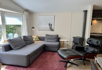 Wohnzimmer eines kleinen Familienchalets in den Niederlanden mit grauem Sofa, Sessel und Kamin.