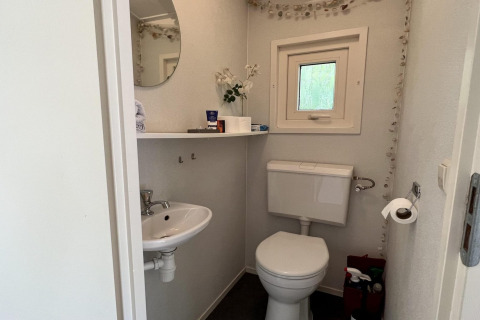Petite salle de bains de chalet familial avec toilettes, lavabo, miroir, étagère et fenêtre. Pays-Bas, proche plage.