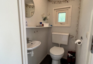 Pequeño baño en cabaña familiar con inodoro, lavabo, espejo, estantería y ventana. Países Bajos, cerca de la playa.