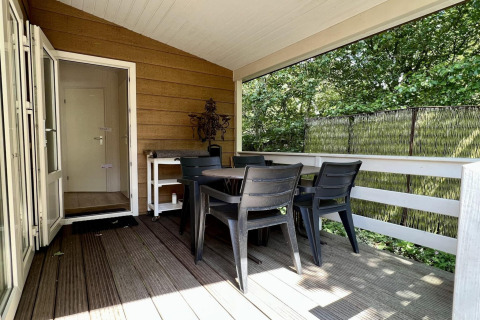 Overdekt terras met tafel en stoelen bij een klein familiechalet vlakbij het strand in Nederland.