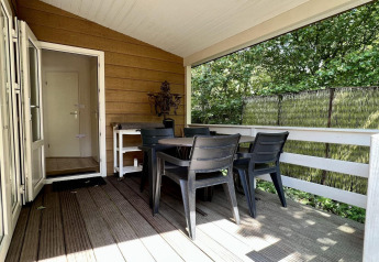 Overdekt terras met tafel en stoelen bij een klein familiechalet vlakbij het strand in Nederland.