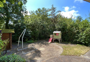 Garten eines kleinen Familienchalets nahe dem Strand in den Niederlanden, mit Spielhaus und Rutsche.