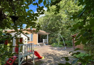 Kleine gezinschalet dicht bij het strand in Nederland met speeltuin, schommel en groene omgeving.