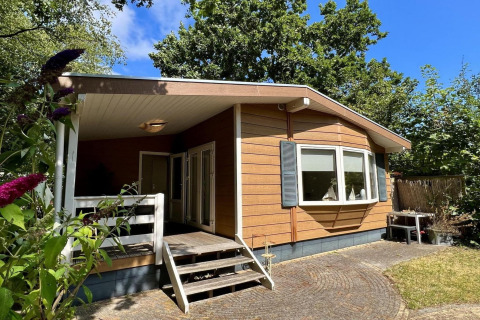 Kleines Familienchalet nahe dem Strand in den Niederlanden, aus Holz, umgeben von Bäumen und Garten.