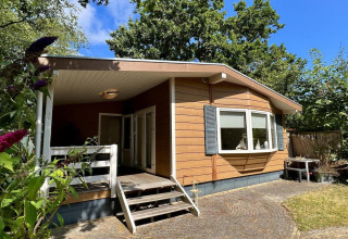 Klein familiechalet dicht bij het strand in Nederland, houten gevel, veranda en groene tuin.
