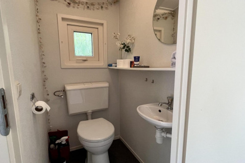 Kleine badkamer in een gezinschalet dicht bij het strand in Nederland met toilet, wasbak en raam.