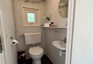 Kleine badkamer in een gezinschalet dicht bij het strand in Nederland met toilet, wasbak en raam.