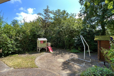 Tuin met speelhuisje, rode glijbaan, schommelrek en groene begroeiing bij een familiechalet in Nederland.