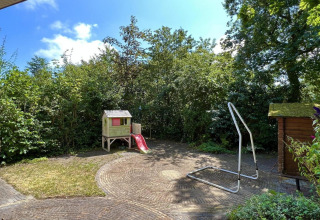 Jardin avec maisonnette de jeu, toboggan rouge, cadre de balançoire et verdure, près d’un chalet aux Pays-Bas.