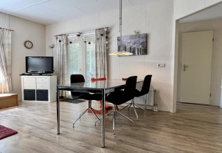 Lichte leefruimte in een klein familiechalet dicht bij het strand in Nederland met tafel en tv.