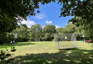 Zonnige speeltuin met grasveld, metalen speelstructuur en bomen bij familiechalet dicht bij het strand in Nederland.