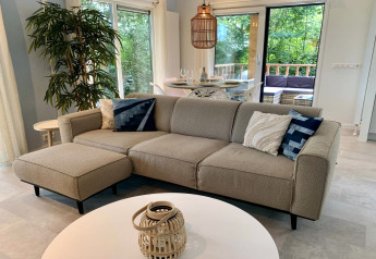 Moderne chalet in Nederland met beige bank, eettafel, grote ramen en uitzicht op het terras.