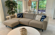 Lyst og moderne chalet i Holland med beige sofa, spisebord, store vinduer og udsigt til grøn terrasse.