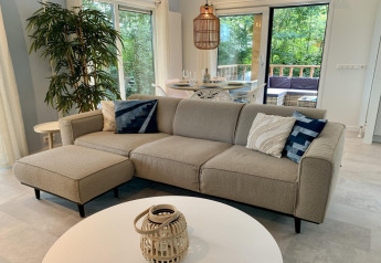 Lyst og moderne chalet i Holland med beige sofa, spisebord, store vinduer og udsigt til grøn terrasse.