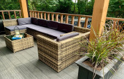 Moderne chalet-terras in Nederland met rotanmeubilair, paarse kussens en groene planten.