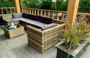 Moderne chalet-terras in Nederland met rotanmeubilair, paarse kussens en groene planten.
